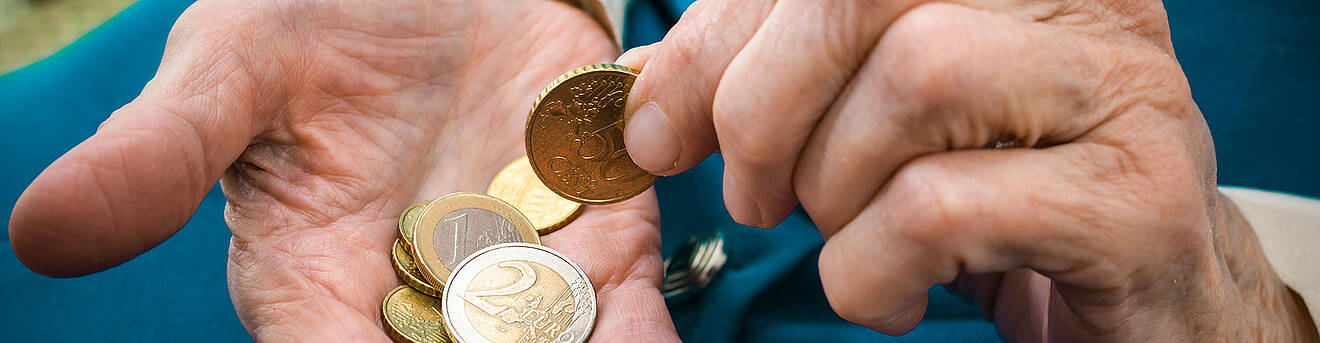 Eine geöffnete Hand mit Münzen, aus der eine Münze mit einer anderen Hand herausgenommen wird Eine geöffnete Hand mit Münzen, aus der eine Münze mit einer anderen Hand herausgenommen wird